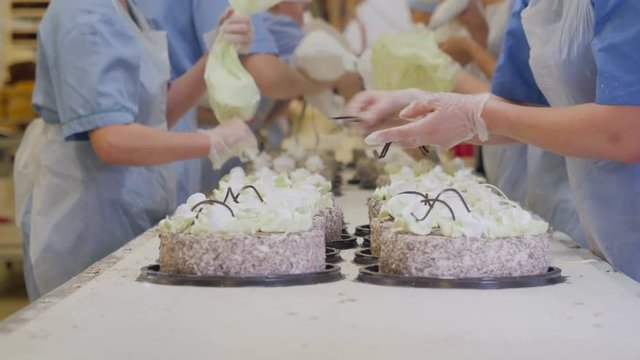 Cakes on a conveyor. Workers decorating cakes at a cake factory. Busy day at confectionery plant. 4K.