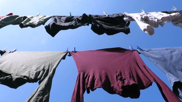 two clothesline with clothespin in colorful shirts adult and baby clothes moving by wind over blue sky 
