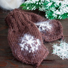 Baby knitted mittens with brown snowflake on a wooden table, selective focus