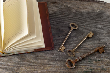 antique book and old keys over rustic wooden background.
