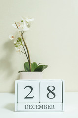 Closeup white wooden calendar with black 28 december word with white orchid flower on white wood desk and cream color wallpaper in room textured background , selective focus at the calendar