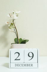 Closeup white wooden calendar with black 29 december word with white orchid flower on white wood desk and cream color wallpaper in room textured background , selective focus at the calendar