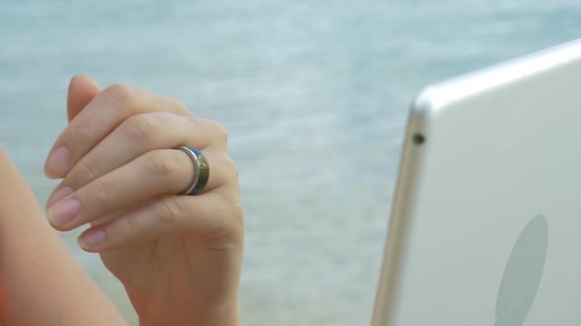 Close-up shot of a woman using smart bluetooth ring to control laptop while working on the beach