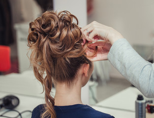 Hairdresser makes hairstyle close-up on blond hair of beautiful woman