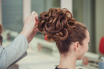 Fototapeta premium young woman making high bun hairstyle at hairdresser indoor shot