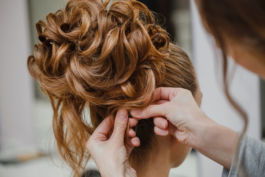 Hairstylist makes the bride with blond hair beautiful high hairdress at the salon