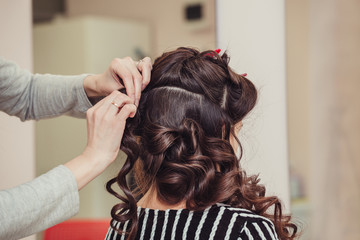 Fototapeta premium Close up of hands of professional hairdresser at beauty salon, curling female hair