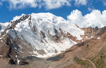 Obraz premium Grandiose view of the snow peak on the background of blue sky with clouds. Moraine lake and the base camp are at the foot of the mountain. Tian Shan mountains, Kazakhstan.