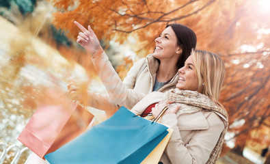 Two beautiful girls in autumn park after shopping. Consumerism a