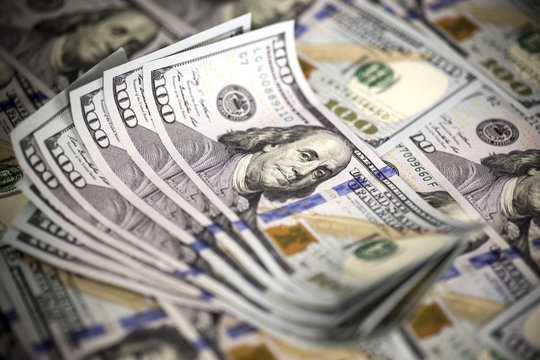 Several modern hundred us dollar bills, slightly curved upward, lying on the background of hundred us dollar banknotes. Close up image. Selective light. Selective focus. 
