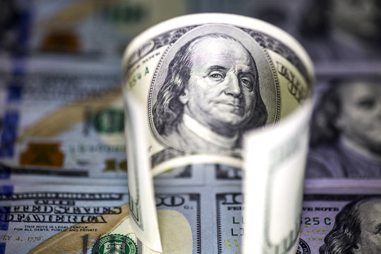 Round curved hundred us dollar bill standing on the background of hundred dollar banknotes, selective light and focus.
