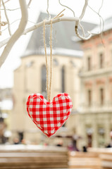 heart made by hand made hanging on a branch in the snow against on the background of the old town buildings. Valentines day. Hand embroidered decoration. Love in the old town.