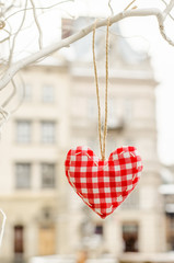 heart made by hand made hanging on a branch in the snow against on the background of the old town buildings. Valentines day. Hand embroidered decoration. Love in the old town.