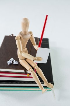 Wooden figurine sitting on a pile of books writing on a paper