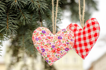 two hearts made by hand hanging on a green Christmas tree on the background of the old town buildings. Valentines day. Hand embroidered decoration.