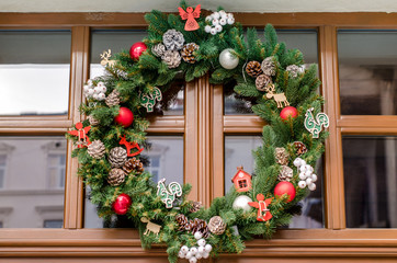decorative green handmade wreath with cones and wooden cockerels with angels from a tree hanging on a background of the old wooden windows