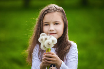 Little girl smelling a white dandelions in spring park