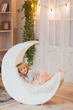 Little girl lying in a wooden bed in the shape of the moon