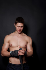 Fototapeta na wymiar Sports boxer man pulls on the hand wrist wraps. Caucasian male model isolated on dark background.