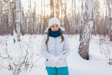 Cute teen girl in a white hat with ear flaps smiling in winter park.