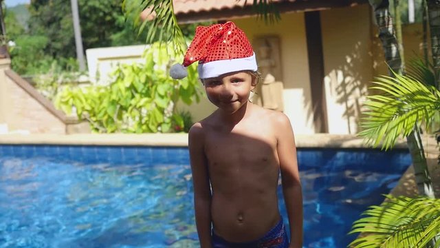 Portrait of little boy in the hat of Santa Claus standing at the pool in slow motion on his traveling of Koh Samui. Thailand. 1920x1080