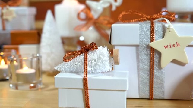 Festive Christmas gifts and gift wrapping in copper and white theme, with candles and ornaments on a natural wood table, close up dolly pan.