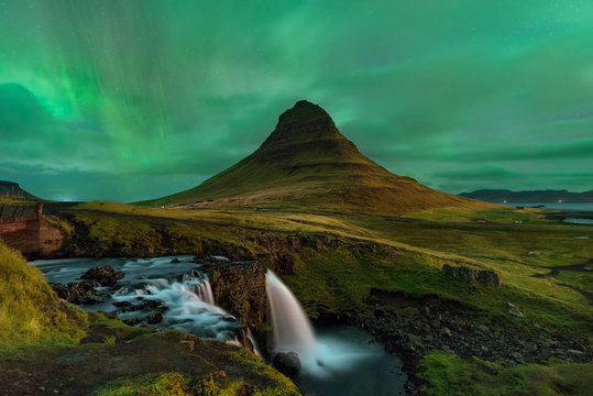 Aurora Boreal sobre o monte Kirkjufell. Paisagem paradisiaca com as famosas cascatas de Kirkjufellsfoss.