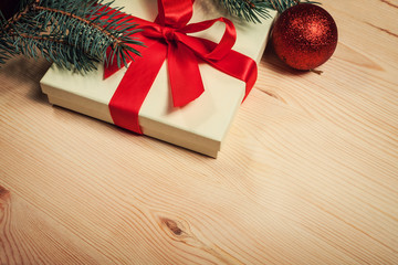 Christmas gift wrapped in red ribbon with fir twig on wooden background