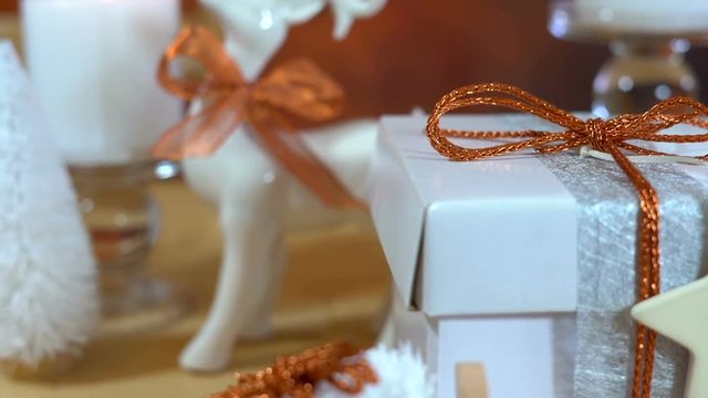 Festive Christmas gifts and gift wrapping in copper and white theme, with candles and ornaments on a natural wood table, close up panning handheld.