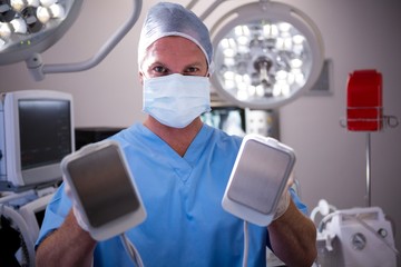 Portrait of male surgeon holding defibrillator - obrazy, fototapety, plakaty