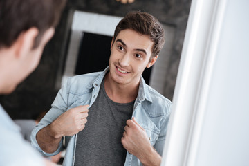 Smiling young man looking at himself in a mirror