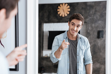 Smiling young man pointing finger at his mirror reflection