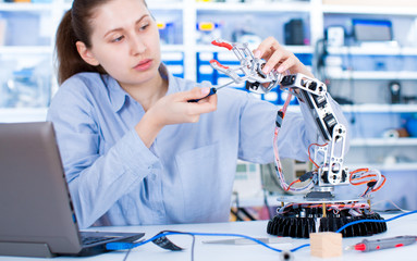 Girl in robotics laboratory. Young woman technician repair roboter manipulator