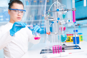 Attractive young female scientist working in laboratory.  Woman scientist looking at a red test tube in a lab. Young woman in chemical lab