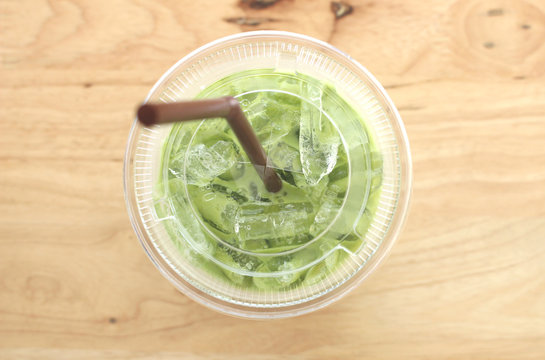 Take away glass of Ice milk green tea with selective focus on the drink and ice inside on wood background from top view shot
