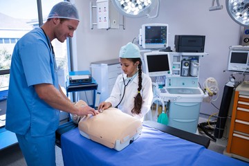 Doctor assisting girl in examining on dummy with stethoscope