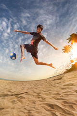Beach soccer player in action. Sunny beach wide angle and sea