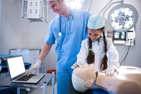 Doctor using laptop while girl examining a dummy
