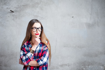 Portrait of thoughtful woman in the red checkered shirt with eyeglasses on the gray textured wall background. Image with copy space