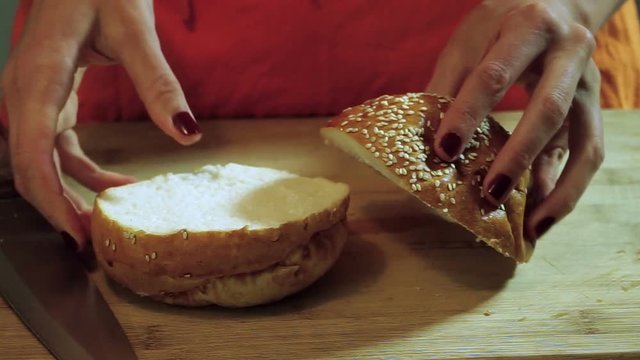 Cooking hamburger. Women's hands cutting the bread rolls with sesame seeds on the parts. HD