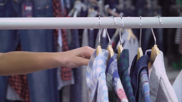 Person man or woman choosing shirt in the store. Close up details hand holding clothes on the rack. Hanger standing in the shop with colored garment.