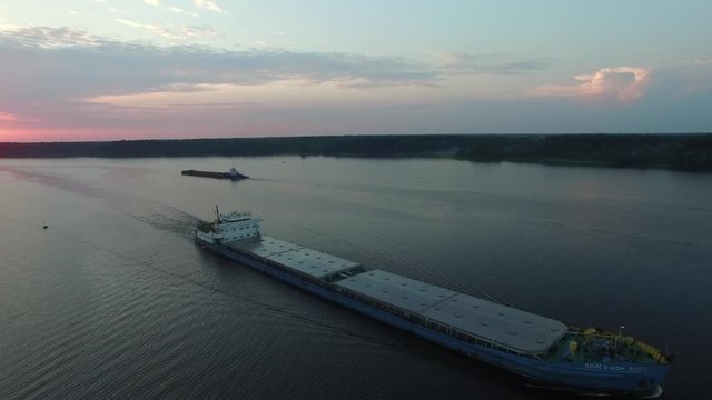 Cargo transport ship sailing on a wide river. Summer dawn. The camera movesh in the air away from the vessel. Another barge in background. Transportation on the river. Aerial view.