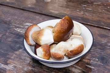 Peeled and washed boletus in metal bowl on wet old table