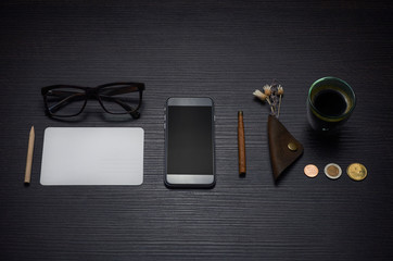 Smart phone, cigarillo, coins, coffee, glasses and card on the w