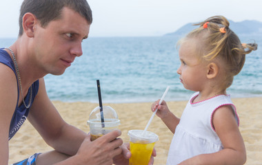 Dad and daughter drinking juice on the beach