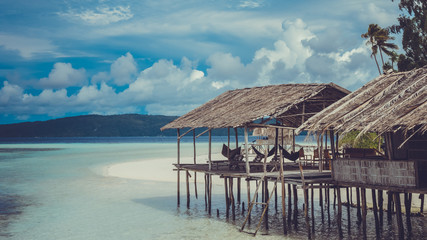 Water Hut of Homestay on Sandy Bank, Clouds in Background - Kri Island. Raja Ampat, Indonesia, West Papua