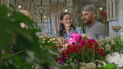 Couple of customers choosing bouquet in flower shop. Floral designer showing them beautiful composition and they buying it