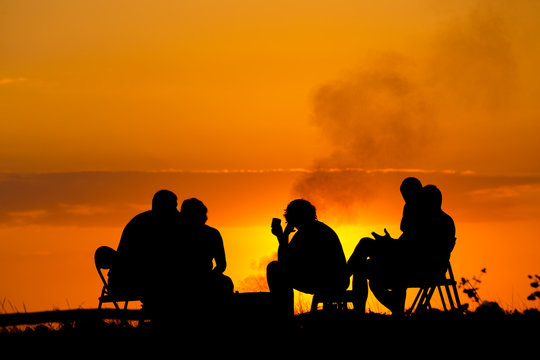 people in camping sitting near campfire against sunset