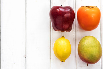 four different fruits apple persimmon lemon and mango on wooden white by lines