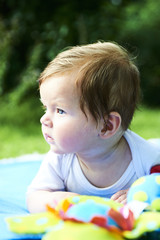 Newborn girl with blue eyes in the beautiful park outdoors, lies on a blue blanket with some toys and looking around.